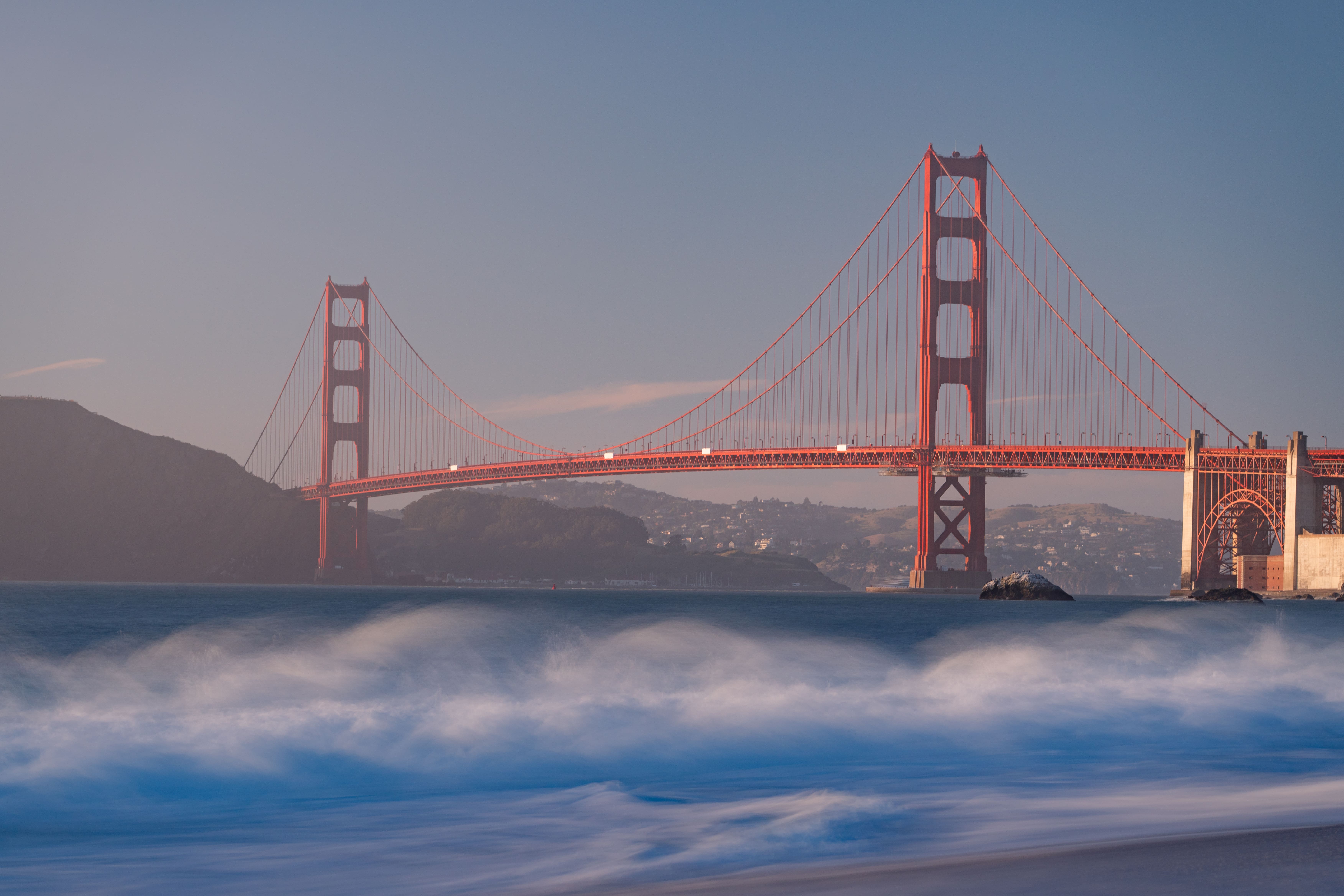A long-exposure shot of the Golden Gate Bridge by the waves of Baker Beach